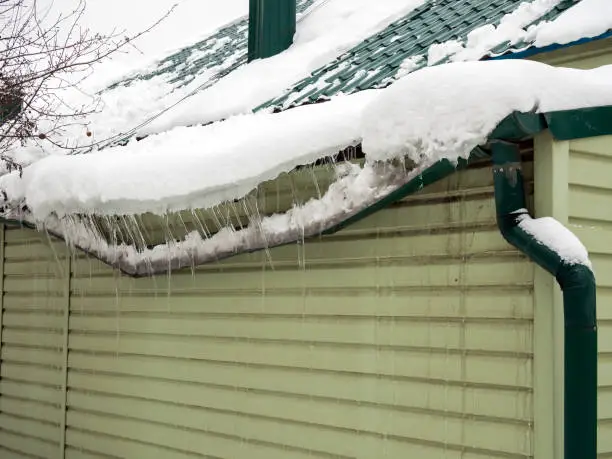A suburban home with snow on the roof and large icicles forming along the gutters — showing the early signs of ice dams that can cause roof damage if not prevented.